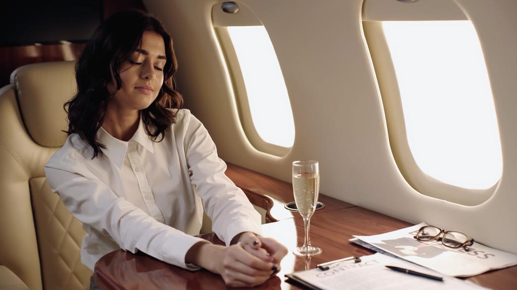 Young businesswoman sitting near champagne and newspaper in private plane  - Foto, Imagen