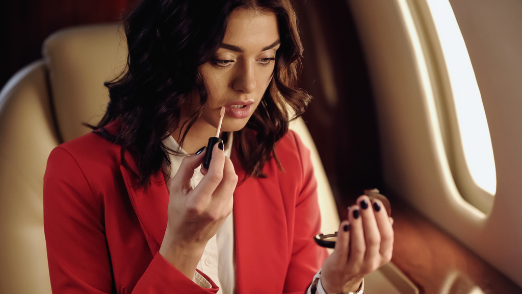 Businesswoman applying lip gloss and holding mirror in private plane  - 写真・画像