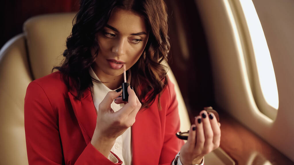 Businesswoman applying lip gloss and holding mirror in private jet  - Zdjęcie, obraz