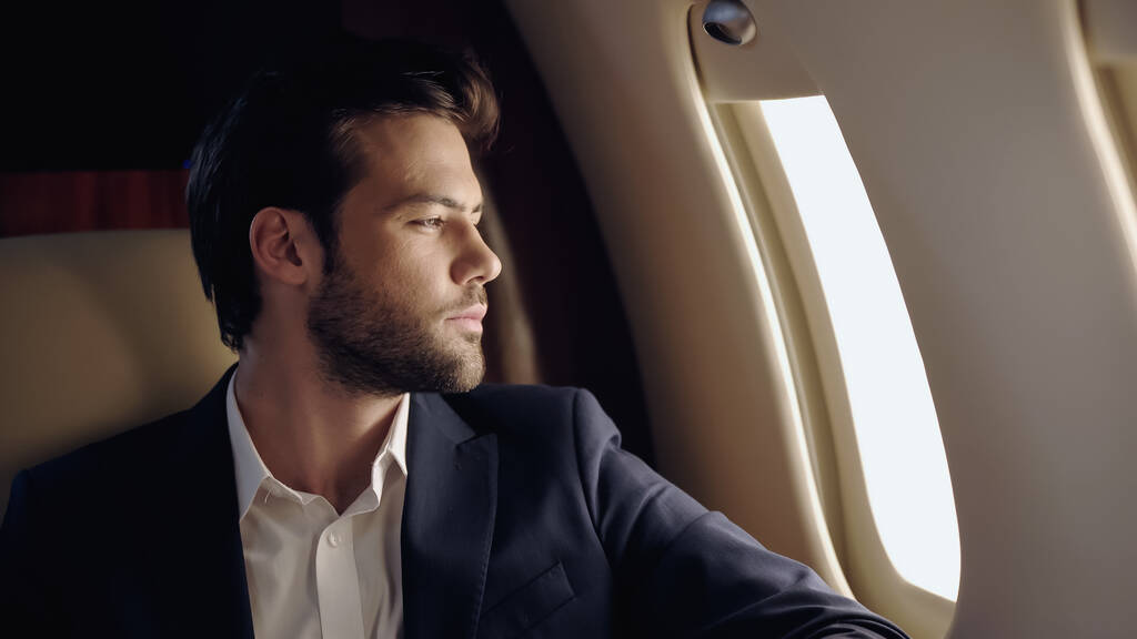 Homme d'affaires barbu regardant la fenêtre dans un avion privé  - Photo, image