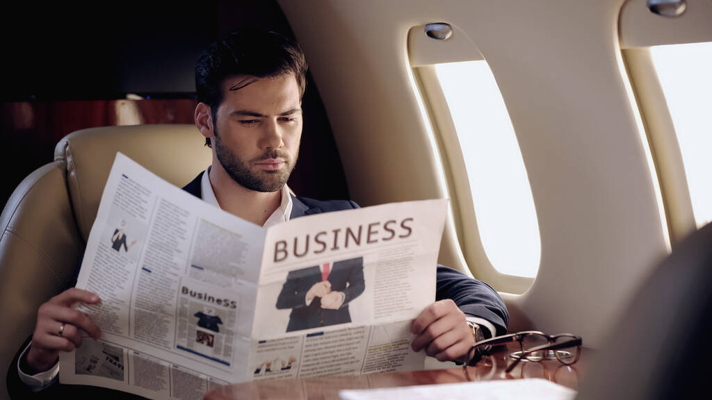 Bearded businessman reading newspaper near eyeglasses in private plane  - Fotó, kép