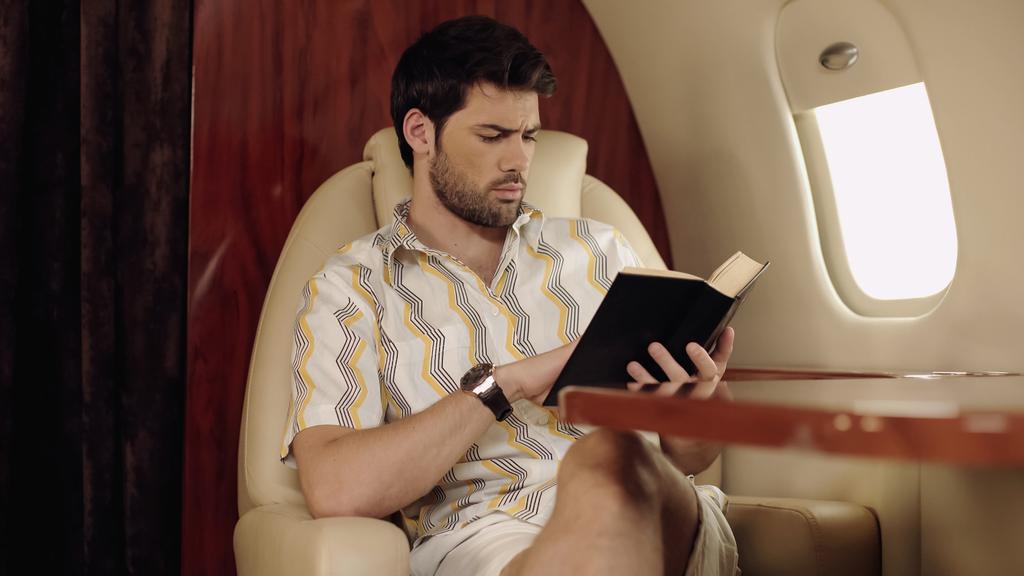 Bearded man reading book while traveling in private jet  - Foto, immagini