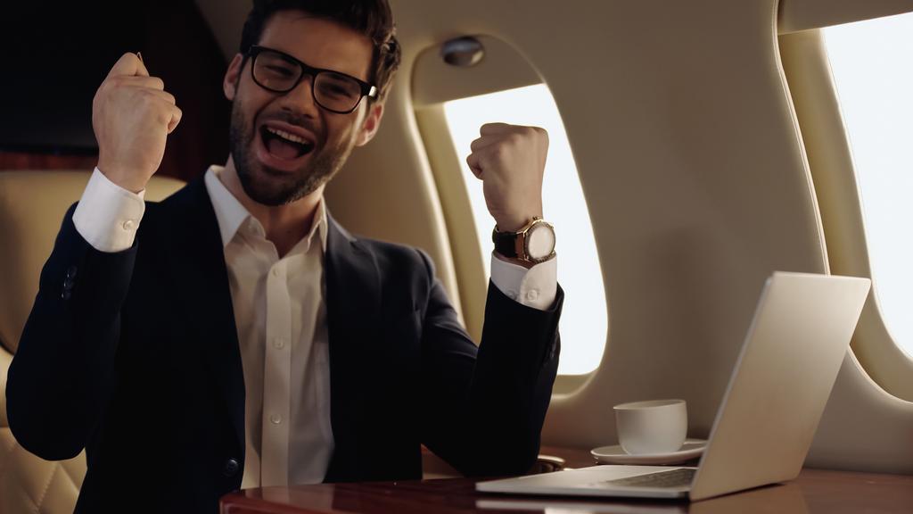 プライベート飛行機でノートパソコンとコーヒーの近くに座って興奮したビジネスマン  - 写真・画像