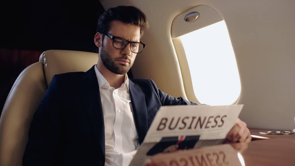Empresario en gafas con periódico borroso en avión privado  - Foto, imagen