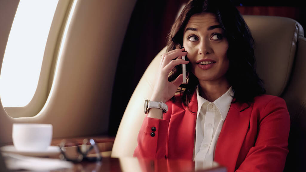 Smiling businesswoman talking on cellphone in private plane  - Фото, изображение