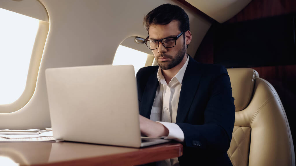 Businessman using blurred laptop near papers in private jet  - Photo, Image