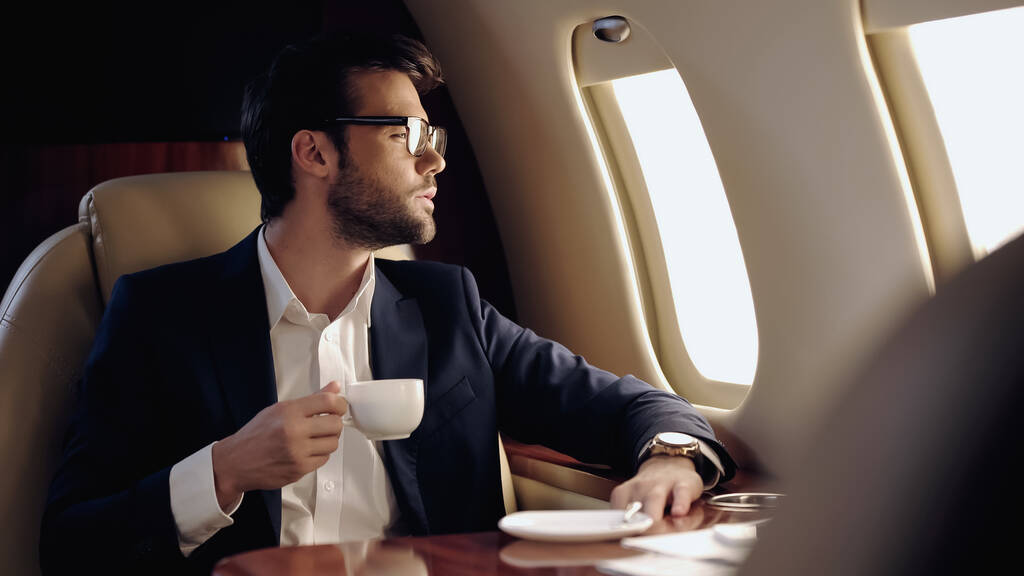 Γενειοφόρος επιχειρηματίας κρατώντας κύπελλο σε ιδιωτικό αεροπλάνο  - Φωτογραφία, εικόνα