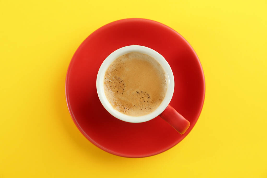 Cup of tasty coffee on yellow background, top view - Photo, image
