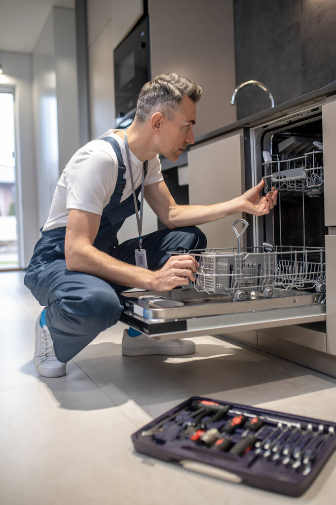 Profile of man crouching looking into open dishwasher - Foto, Imagem