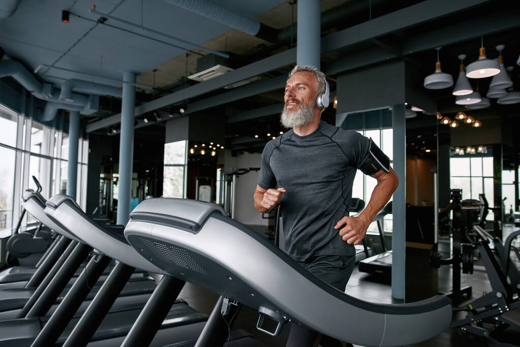 Active senior man jogging on treadmill in sports center - Foto, immagini