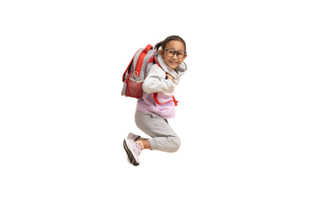Funny asian child girl carry backpack jumping isolated on white background - Фото, изображение