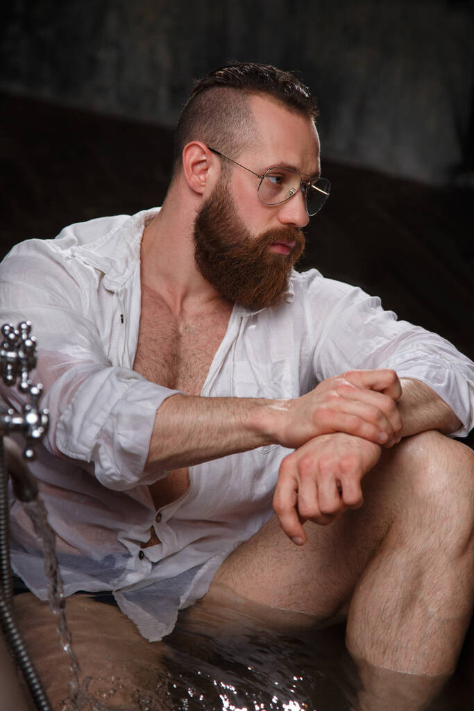 Спортсмен бородатий відпочиває в розкішній ванні в темному інтер'єрі
. - Фото, зображення