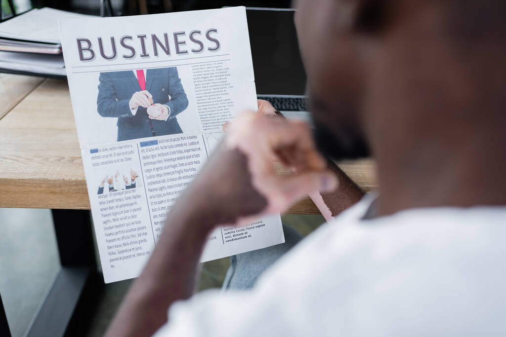 cropped view of blurred african american man with vitiligo skin reading business newspaper in office - Photo, Image
