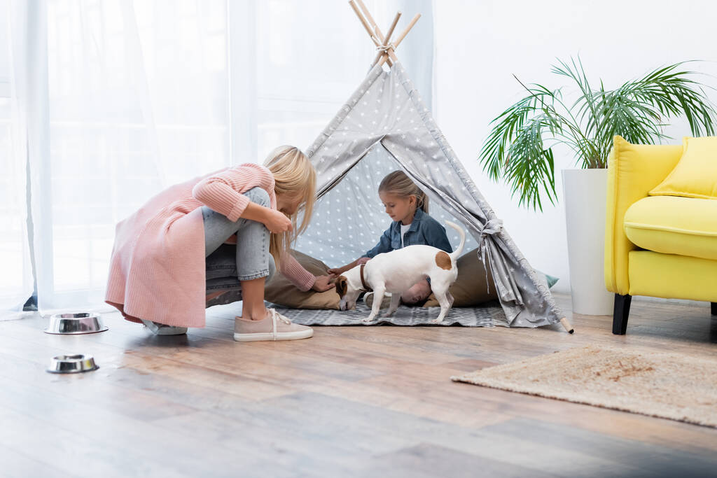 Child sitting in tent near jack russell terrier and mom at home  - Foto, afbeelding