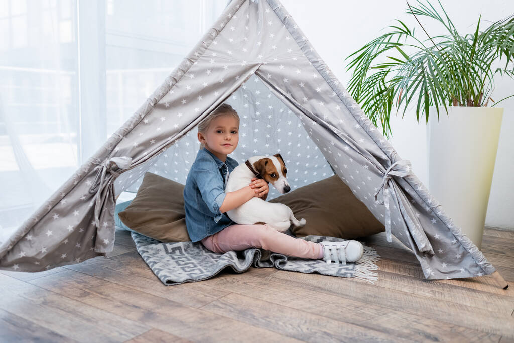 Kid hugging jack russell terrier in tepee at home  - Photo, Image