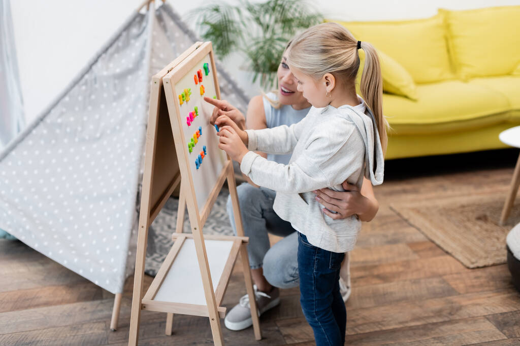 Parent hugging child and pointing at magnetic easel at home  - Foto, immagini