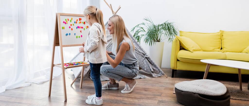Parent and girl standing near magnetic easel at home, banner  - Fotoğraf, Görsel