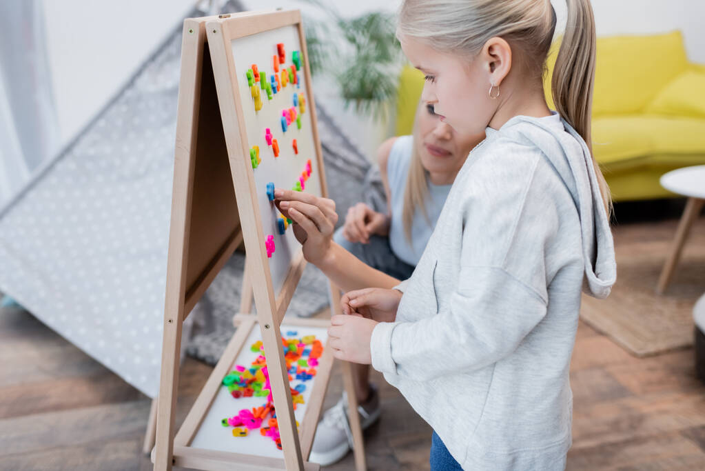 Kid standing near mom putting magnets on easel at home  - Foto, imagen