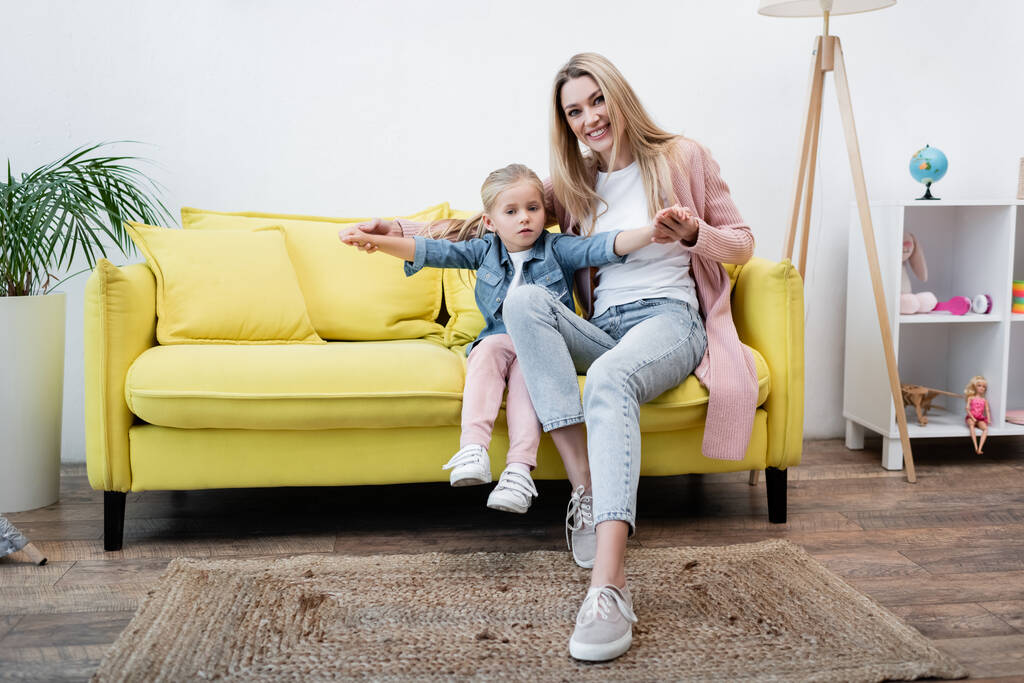 Усміхнена мати тримає руки дитини на дивані вдома
  - Фото, зображення