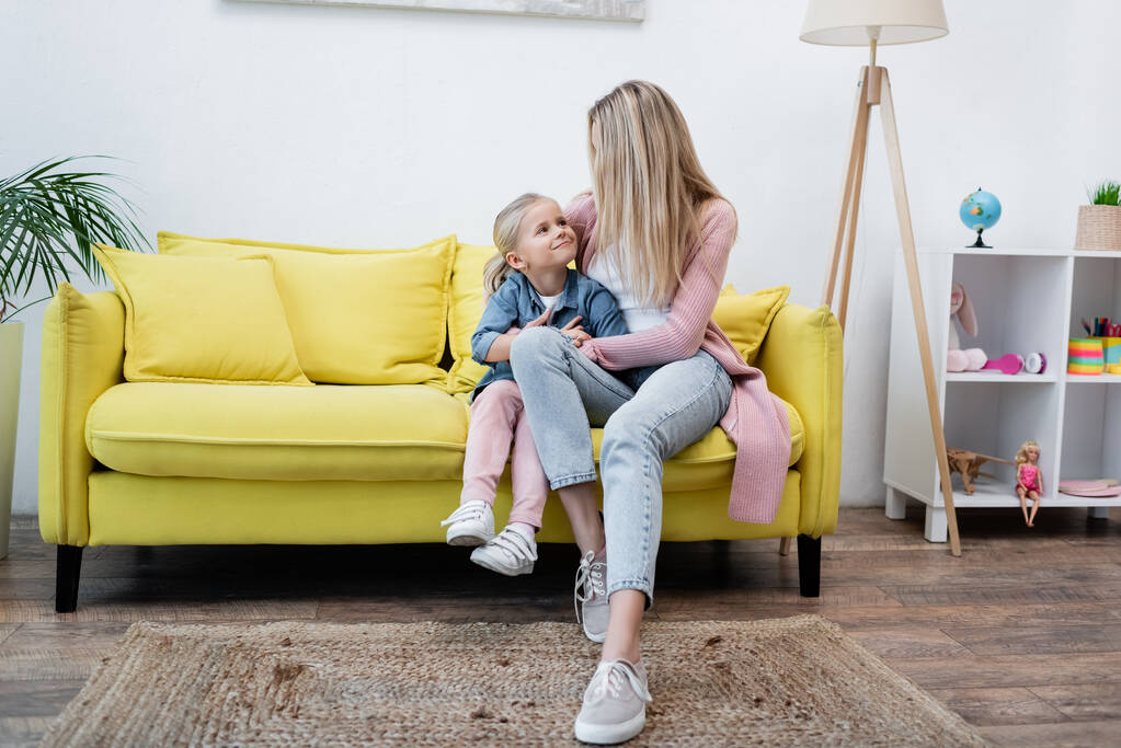 Parent hugging smiling daughter on couch at home  - Fotoğraf, Görsel