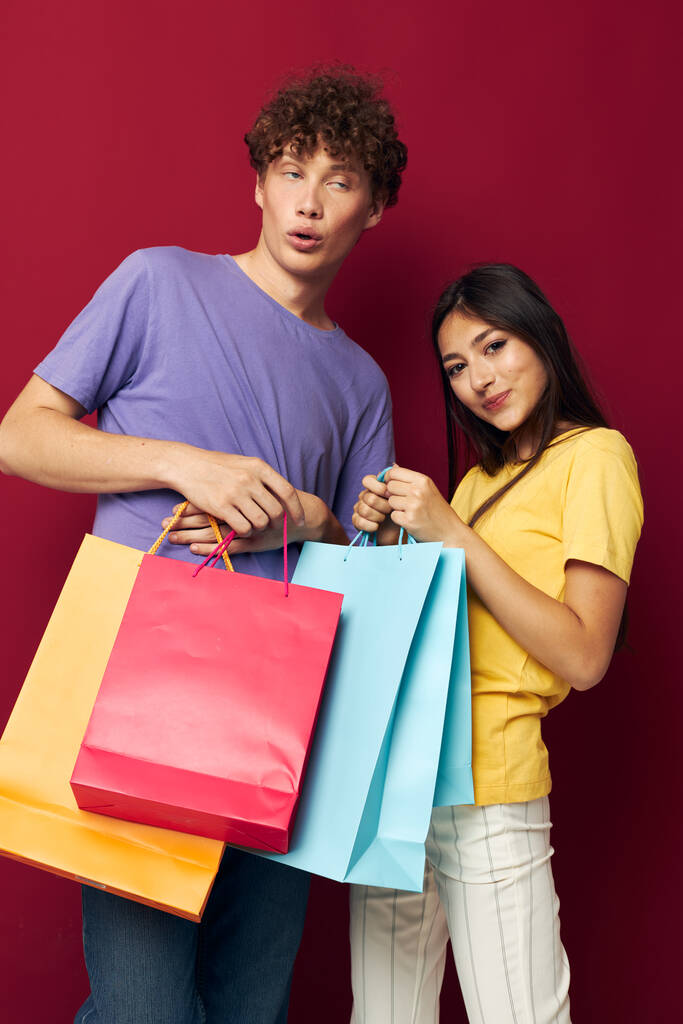 Renkli tişörtler içinde sevimli genç bir çift çantalarla izole edilmiş arka plan alışverişi yapıyorlar. - Fotoğraf, Görsel