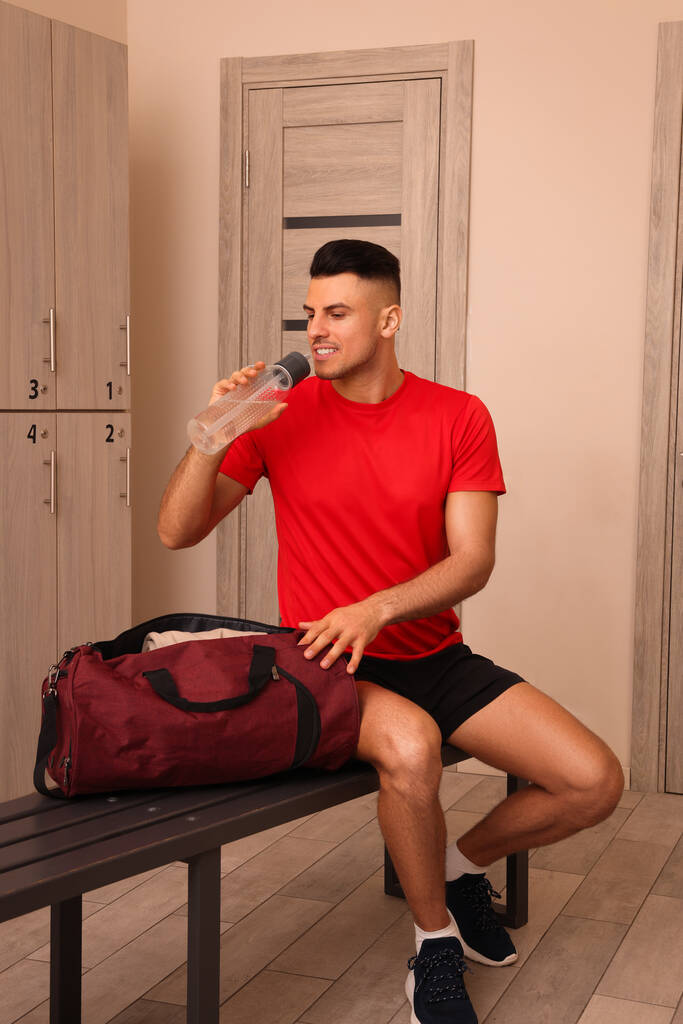 Красивый мужчина пьет воду в раздевалке
 - Фото, изображение