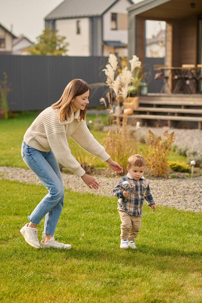 Жінка грає, ловлячи дитину на зеленому газоні біля будинку
 - Фото, зображення