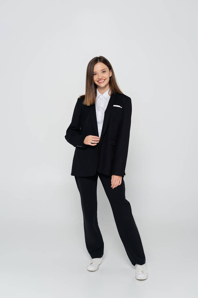 full length of happy and stylish woman in suit on grey - Photo, Image