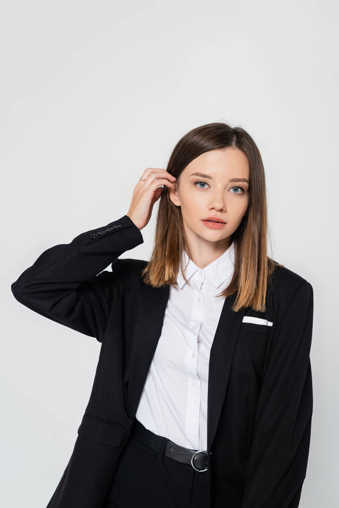 young stylish woman in suit adjusting hair isolated on grey - Fotografie, Obrázek