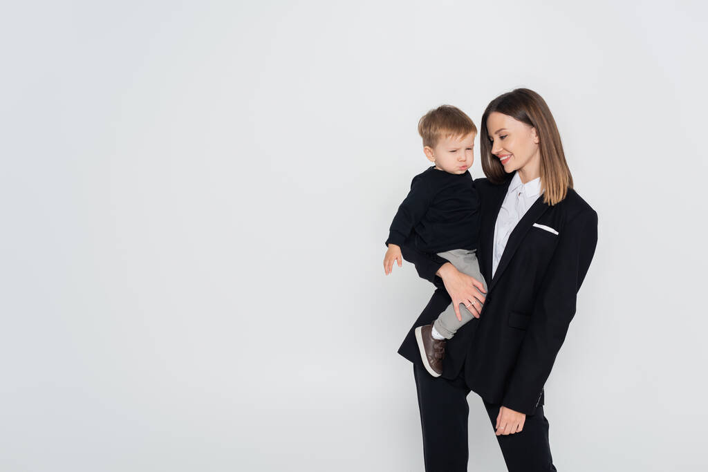 стильна і щаслива мати тримає в руках маленького сина ізольовано на сірому
 - Фото, зображення