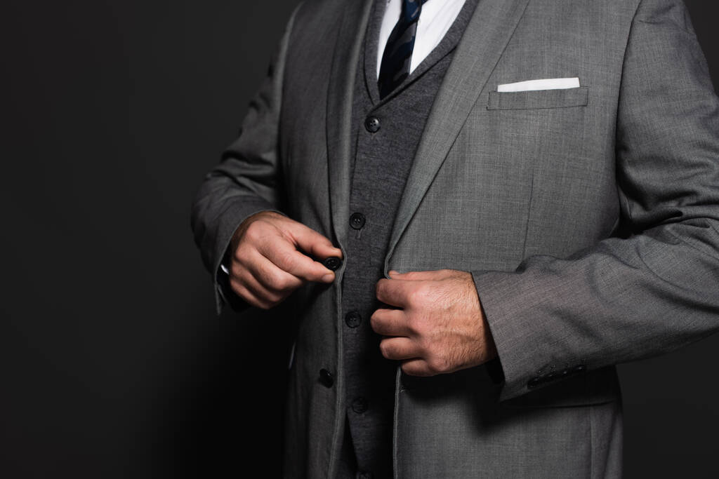 cropped view of businessman buttoning blazer on dark grey background - Foto, Imagen
