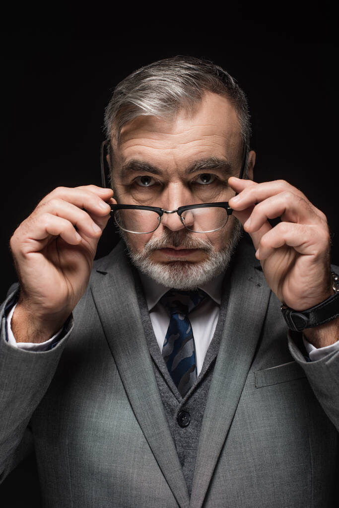 senior bearded businessman holding eyeglasses while looking at camera isolated on black - Fotoğraf, Görsel