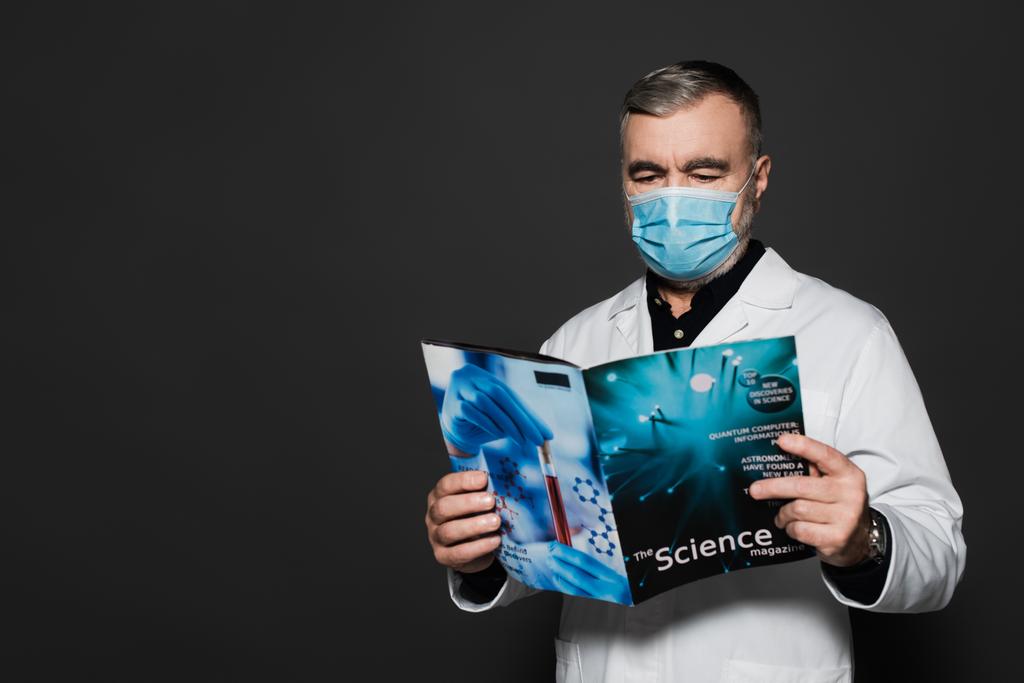 senior physician in medical mask reading science magazine isolated on dark grey - Photo, Image