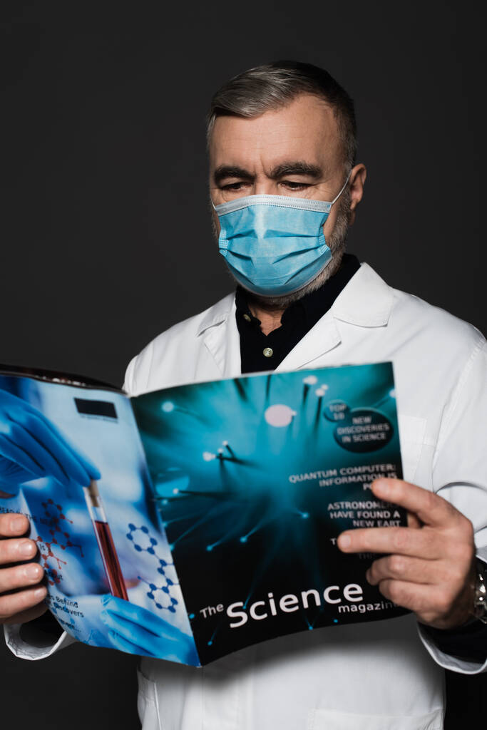 médico en máscara médica lectura ciencia revista aislado en gris oscuro - Foto, imagen