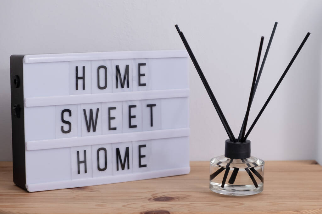 Leuchtkasten mit Text HOME SWEET HOME und Aroma-Schilf-Diffusor auf Holztisch - Bild - Foto, Bild