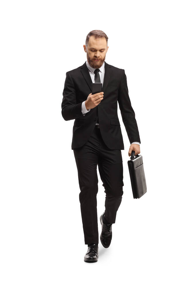 Full length portrait of a young businessman walking and typing on a smartphone isolated on white background - Φωτογραφία, εικόνα