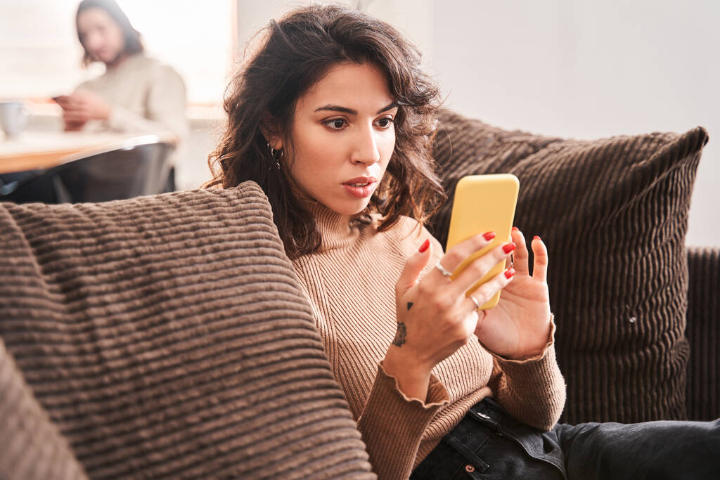 Жінка дивиться на смартфон з здивованими емоціями сидячи
 - Фото, зображення