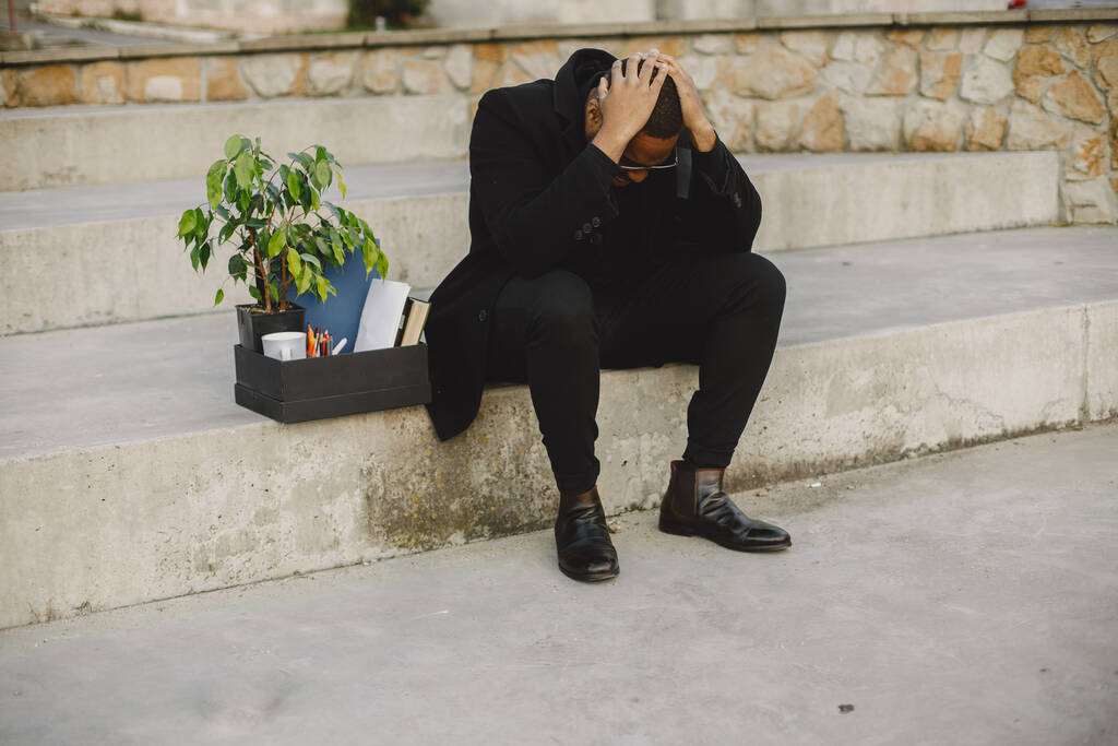 Frustrado negro despedido hombre sentado fuera con caja - Foto, Imagen