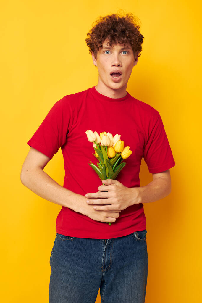 portrait of a young curly man romantic posing with a yellow bouquet of flowers yellow background unaltered - Photo, Image