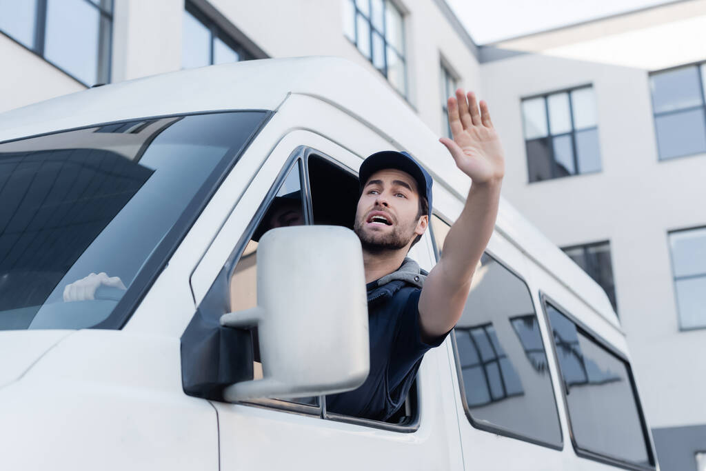 Worried courier waving hand while driving auto  - Foto, Imagen