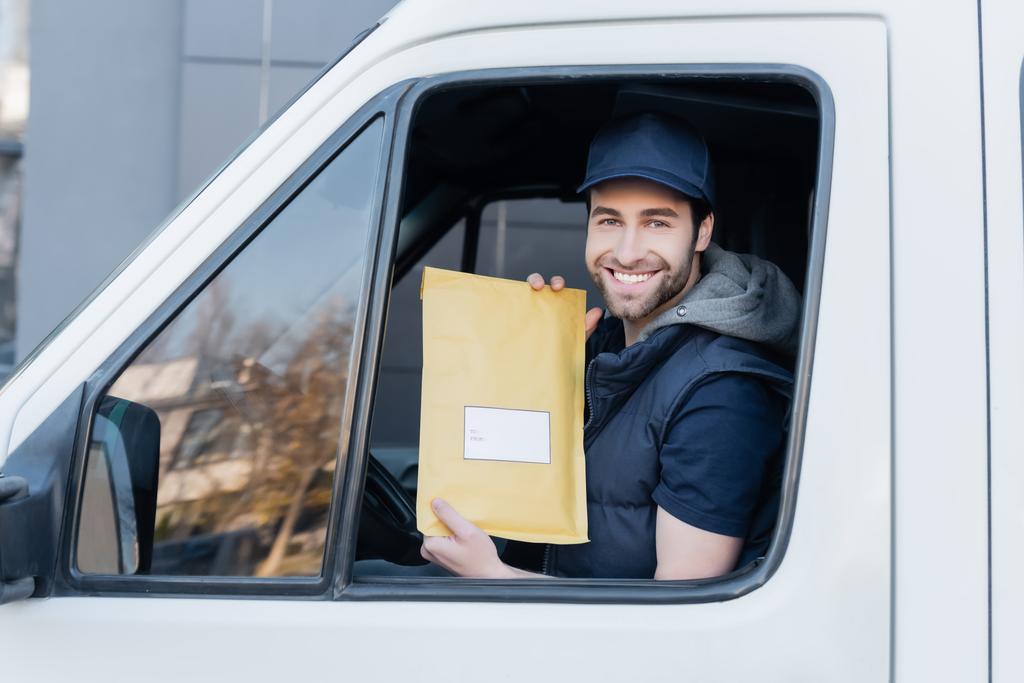 Smiling courier holding parcel and looking at camera in car  - Foto, Bild