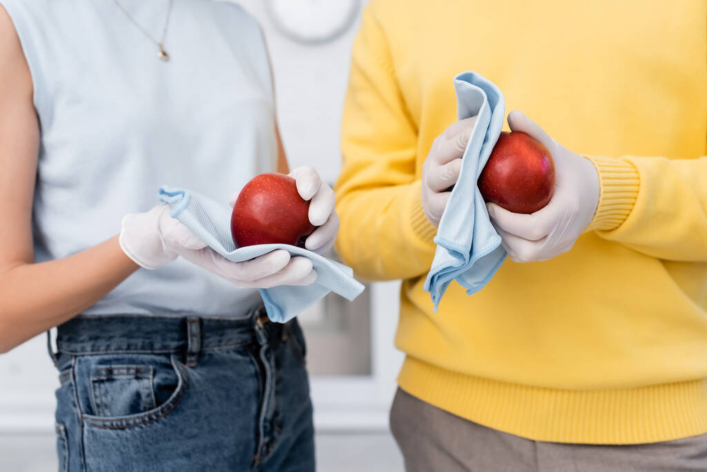 Cropped view of blurred couple in latex gloves cleaning apples in kitchen  - Zdjęcie, obraz