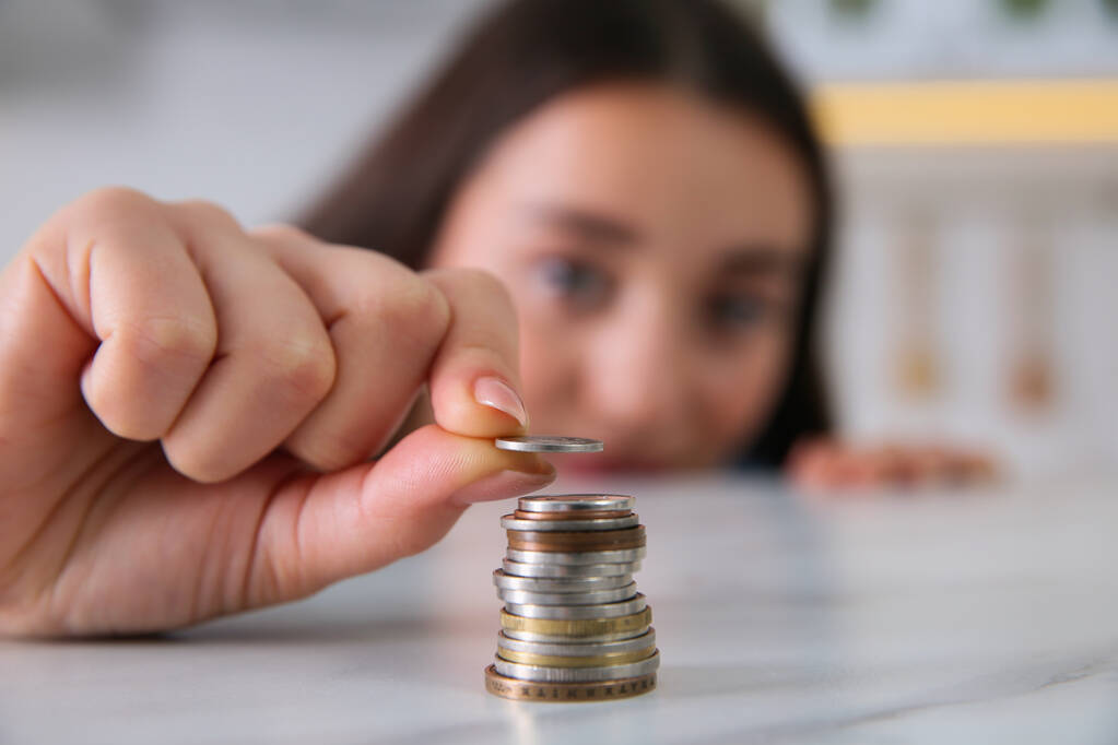 Молода жінка кладе монети за столом, зосереджується на руці. Грошові заощадження
 - Фото, зображення