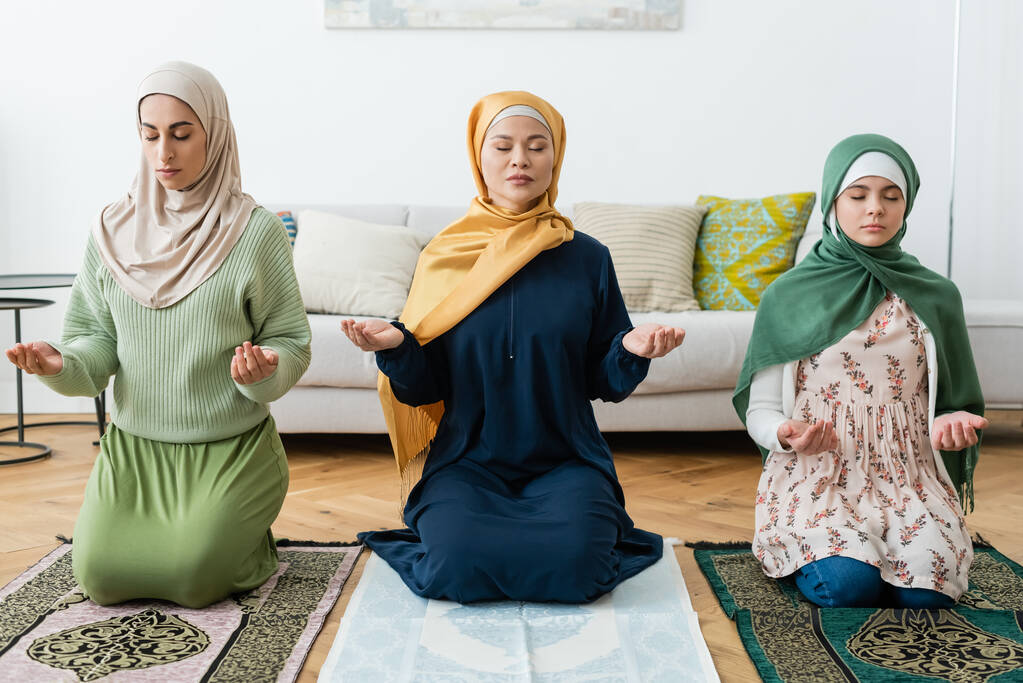 Mujeres multiétnicas y adolescentes rezando con los ojos cerrados en casa  - Foto, imagen