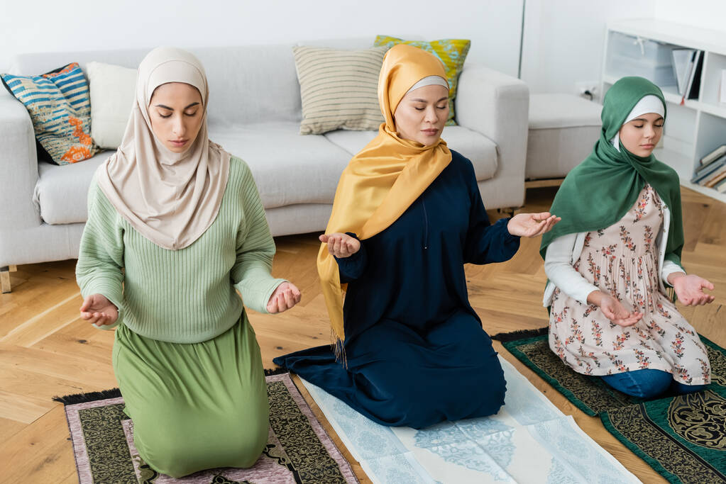 Wieloetniczne kobiety i dzieci modlą się na dywanikach z orientalnym wzorcem w domu  - Zdjęcie, obraz