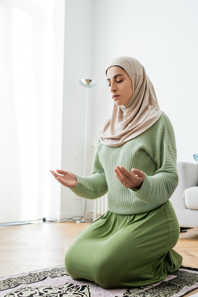Jovem mulher árabe orando no tapete no chão em casa  - Foto, Imagem