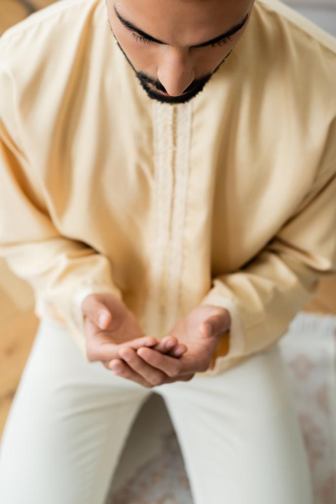 Vista de alto ângulo do jovem homem árabe orando no tapete borrado em casa  - Foto, Imagem