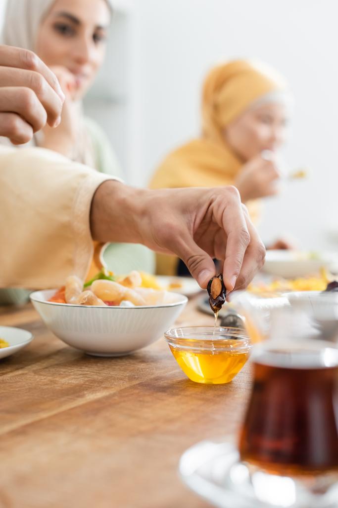 άντρας που βουτάει το μέλι στο δείπνο με θολές διαφυλετικές μουσουλμάνες γυναίκες - Φωτογραφία, εικόνα