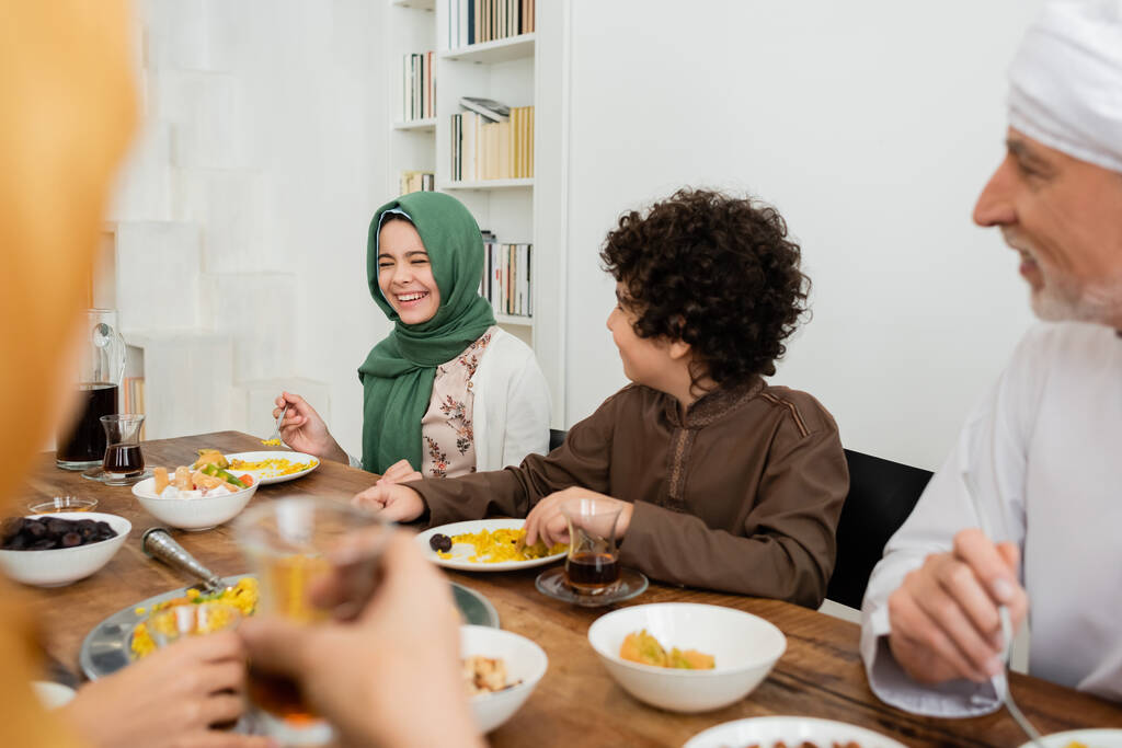cheerful muslim girl laughing during dinner with multiethnic family - Photo, Image