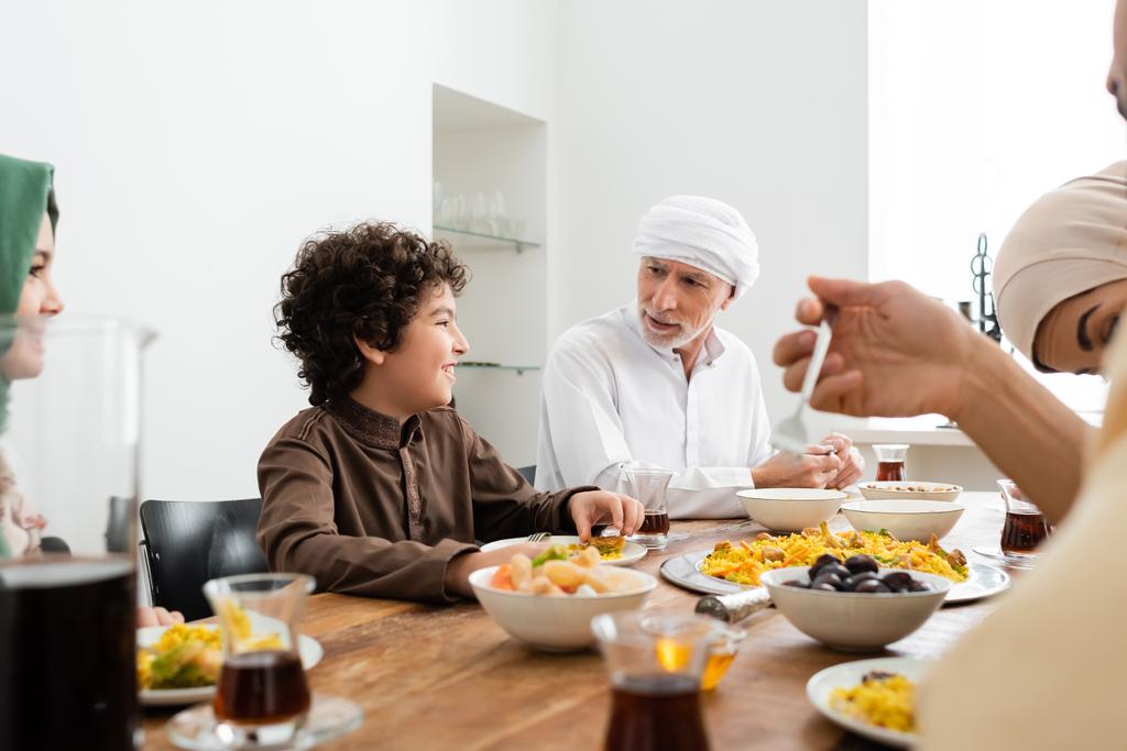 hombre musulmán cenando con nietos multiétnicos felices y familia borrosa - Foto, Imagen